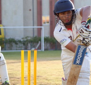 Bild zeigt einen jungen Mann, der Cricket spielt und sich dem Ball mit zischendem Schläger an der indischen High School in Dubai nähert