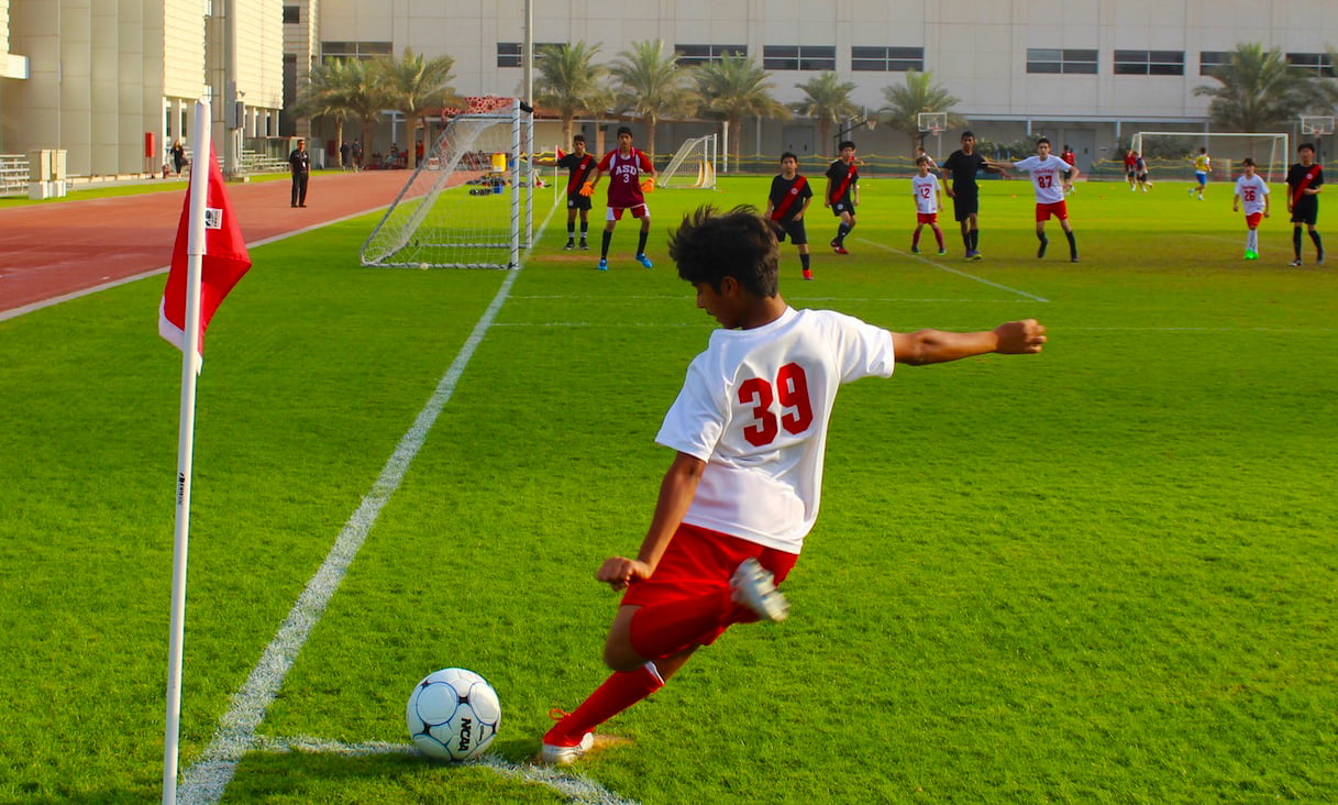 Fußball an der American School of Dubai mit einem Jungen, der mit Teammitgliedern eine Ecke nimmt und darauf wartet, dass der Ball das Tor überquert