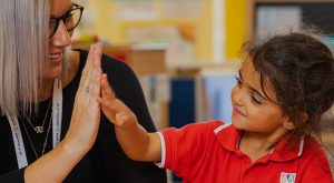 Foto eines glücklichen Kindes und eines Lehrers, die zusammenarbeiten, um ein Problem in der KG-Phase an der West Yas Academy in Abu Dhabi zu lösen