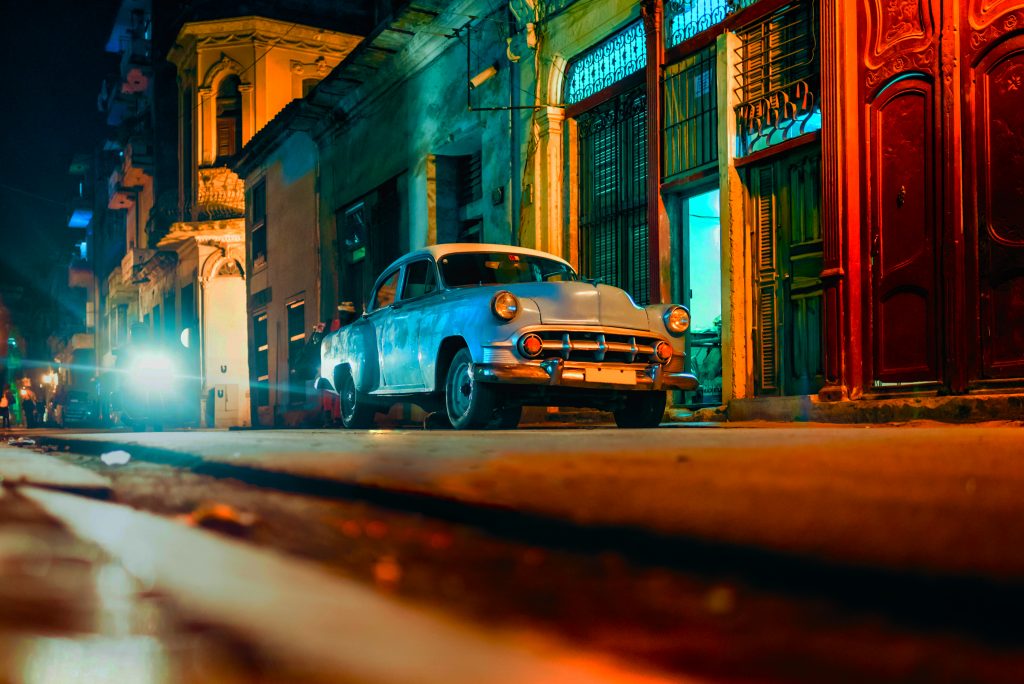 اكتب رسمًا توضيحيًا للفصل الثاني من التحدي الذي يُظهر سيارة قديمة ليلاً مع سماء سوداء مزدحمة بأضواء الشوارع