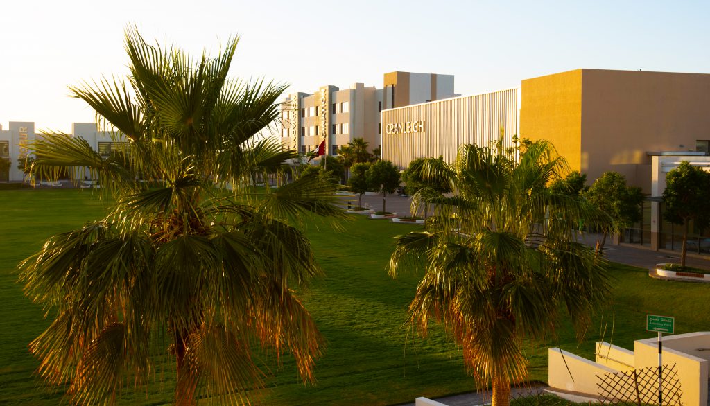 Das Foto des Campus der Cranleigh School in Abu Dhabi im Morgengrauen zeigt die innovative Architektur der Schule und ihre Lage inmitten grüner grüner Sportfelder und Palmen