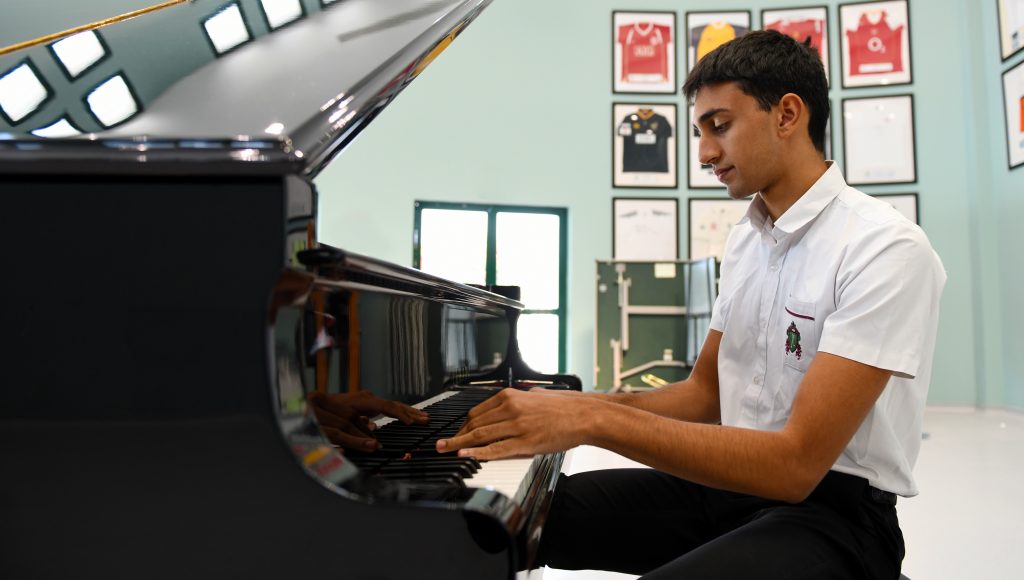 صورة لطالب يعزف على البيانو الكلاسيكي كجزء من تدريب الأوركسترا في كلية جميرا التابعة لجيمس للتعليم في دبي
