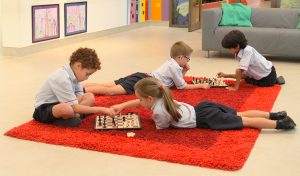 Jüngere Kinder spielen Schach an der Ranches Primary School in Dubai auf einem sehr bequemen feurigen orangefarbenen Teppich!