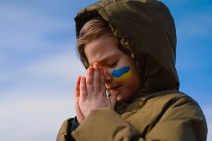 Photo of a child casualty of the Ukraine war praying for peace and the chnace for an education as Minerva's Virtual Academy steps in to offer a free British education to children fleeing war to the UAE