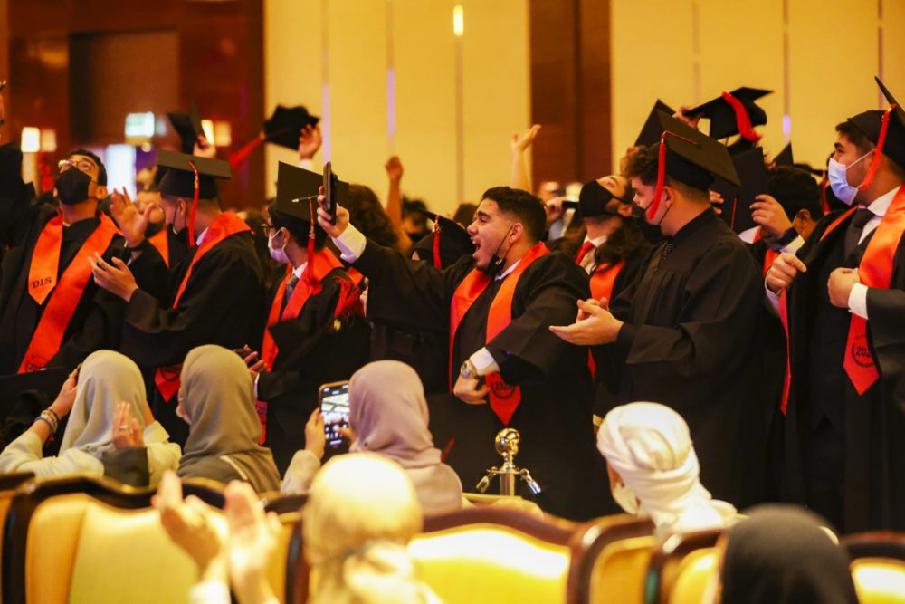 Foto der Ib-Abschlussfeier an der Deira International School Dubai im Jahr 2022 mit vor Freude hüpfenden Schülern, als die Schule ihre herausragenden Ergebnisse einem Publikum stolzer Eltern vorstellte
