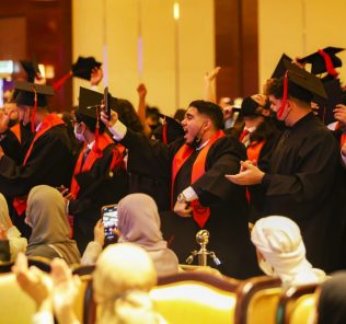 Foto der Ib-Abschlussfeier an der Deira International School Dubai im Jahr 2022 mit vor Freude hüpfenden Schülern, als die Schule ihre herausragenden Ergebnisse einem Publikum stolzer Eltern vorstellte